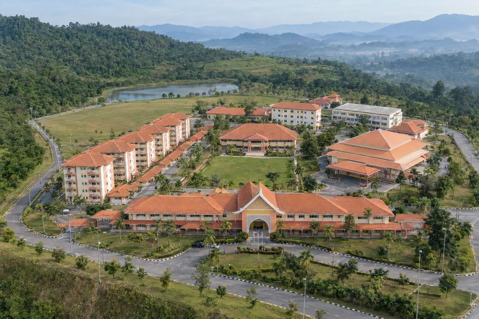 Illustrated aerial view of Kolej Matrikulasi Kelantan: terracotta-roofed blocks around a green field, with forested hills behind.